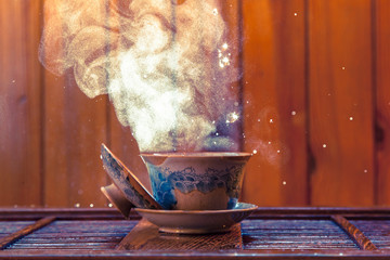 Traditional chinese painted clay tea brewing cup with cloud of steam and splashing hot water on...