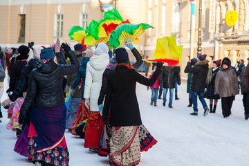 Girls in winter jackets dance on a snowy street with fans. Hare Krishna sectarians