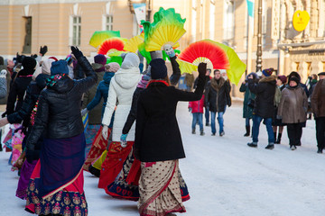 Girls in winter jackets dance on a snowy street with fans. Hare Krishna sectarians