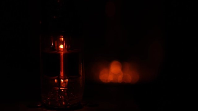 A vacuum tube powering down in the dark. The scene starts with the tube glowing, then the tube slowly powers down as it gets cooler. Shallow depth of field, second tube in back out of focus.