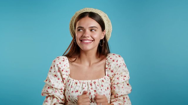Happy european hipster woman dancing, showing yeah gesture of victory, she achieved result, goals. Surprised excited girl in hat on blue background
