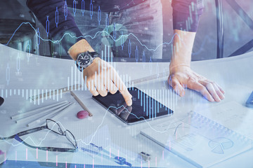 Double exposure of man's hands holding and using a digital device and forex graph drawing. Financial market concept.