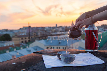 Hands pouring chinese tea into a clay teapot overlooking the sunset city