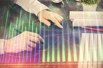 Double exposure of man's hands holding and using a phone and financial graph drawing. Analysis concept.