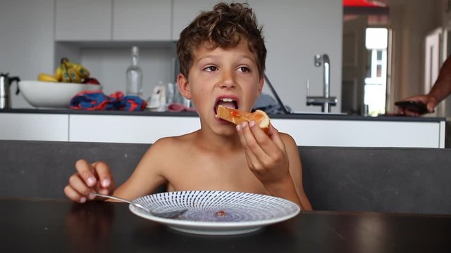 Pretten child boy preparing bread with jelly and taking a bite