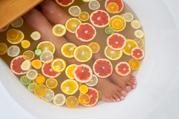 Top view orange, lemon, grapefruit slices and woman legs in bathtub.