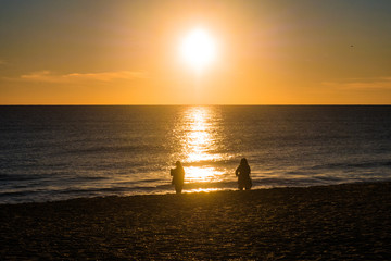 Sunset at the beach with sun in the sky and 2 people in silhouette