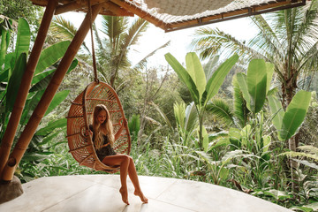 Tourist woman swing on wicker rattan hang chair in the jungle, nature view