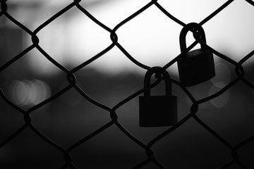 Silhouette of two pad locks on chain link fence