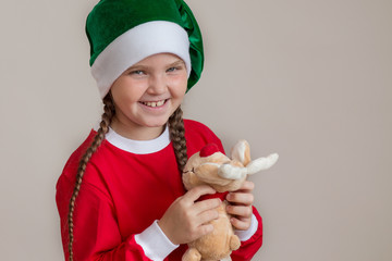 Happy girl in santa costume with deer toy on light gray background 