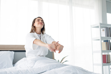 Bright Caucasian woman with stretching after waking up in the morning on the white bed.