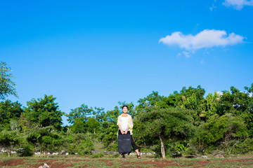 青空と森の背景にいるスーツケースを持った女性