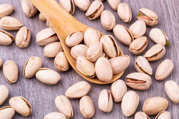 Pistachio in a wooden spoon on grained wood background.