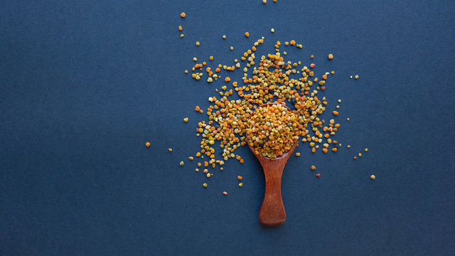 Bee pollen in a wooden spoon healthy food supplements. Close up on a black background. Top view, flat lay. copy space for text.