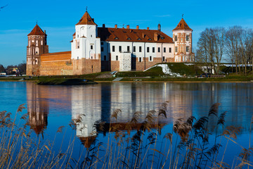 Fototapeta na wymiar View of architectural ensemble of Mir Castle from pond in sunny winter day, Grodno region, Belarus