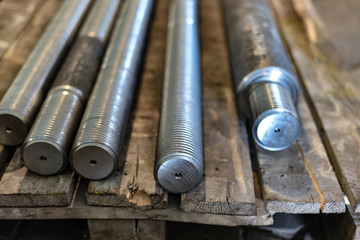 After turning and milling, the threaded studs lie on a wooden rack in the warehouse.