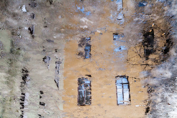 Vintage house windows reflected in a muddy puddle