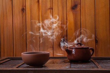 Traditional chinese teapot  and teacup with a cloud of steam on a wooden background