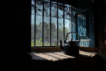 Old and vintage black kettle kept near the window from where sun rays are peeping in.