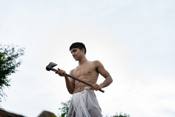 Young handsome shirtless boy holding axe in his hands.