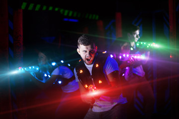Fototapeta na wymiar Portrait of guy in colored beams of laser guns during laser tag game on dark arena