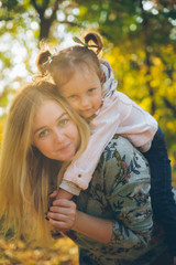 piggyback mother playing with daughter at autumn city park