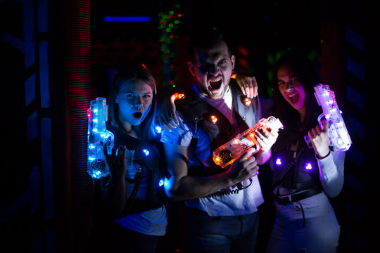 Group portrait of young people with laser guns having fun on dark lasertag arena