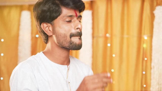 Hands feeding or giving sweet to young man in tradtional dress and eating laddu or sweet on Diwali festival or wedding ceremony ceremony