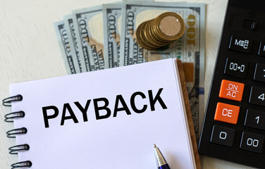 PAYBACK word in a notebook with a pen against the background of dollar bills
