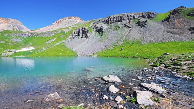 Panoramic panning view on cold colorful water of Ice Lake and Mineral Creek on hiking trail in Silverton, Colorado in San Juan Mountains summit peak with snow