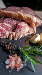fresh slices of raw meat steak pork beef on black slate stone plate background with ingredients spices salt pepper garlic rosemary preparing and marinating barbecue meat. Healthy, natural food.
