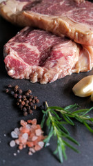 fresh slices of raw meat steak pork beef on black slate stone plate background with ingredients spices salt pepper garlic rosemary preparing and marinating barbecue meat. Healthy, natural food.