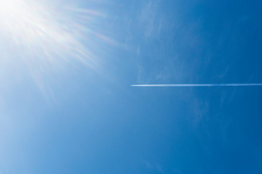 Blue sky and light from the sun and the faint shadow of a plane flying in the sky.