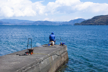 青空の堤防で釣りをする人物（後ろ姿）の写真釣り人｜撮影地伊豆日本