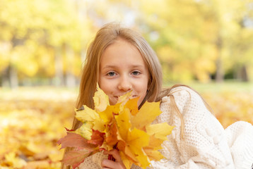 Naklejka na ściany i meble beautiful blonde teen girl sitting on the grass in an autumn Park with maple trees