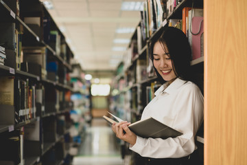 Young Asian women are searching for books and reading from the bookshelves in the college library to research and develop themselves in education