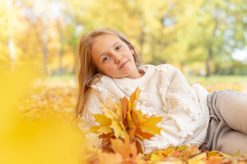 beautiful blonde teen girl sitting on the grass in an autumn Park with maple trees