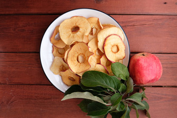 Organic Apple chips (slices) on a wooden background on a white plate are a healthy vegetarian fruit snack or cooking ingredient.  The concept is a healthy diet. Top view