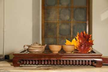 Chinese kettle and tea cups on vintage wooden table with autumn leaves and cloud of vapor