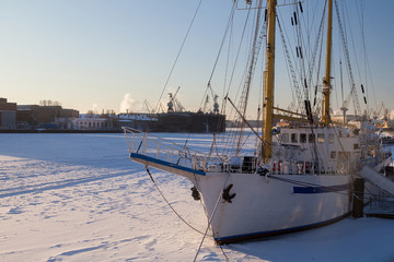 A white sailboat in the winter parking is frozen into the ice. Training ship. Saint Petersburg
