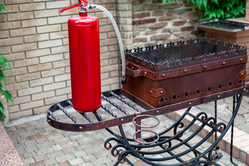 Red fire extinguisher stands on metal barbecue