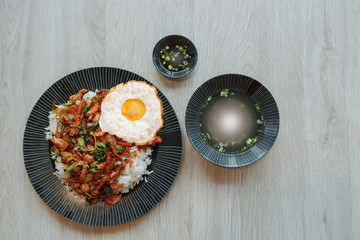 Flat lay of rice topped with stir-fried  pork and basil with fried egg and soup on wooden table, Thai popular street food concept