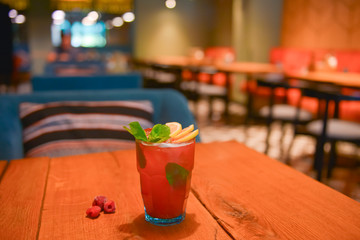 Red fruit cocktail drink with raspberry, mint and ice on dark rustic wooden table in a bar or restaurant.