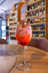 A glass with the red citrus cocktail. Alcohol summer beverage in a wine glass. Refreshing drink with ice.