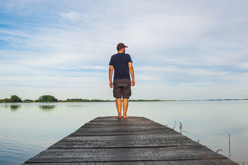 Man in short cargo pants standing on wooden pier and observing the surface of lake, Varazdin lake,...
