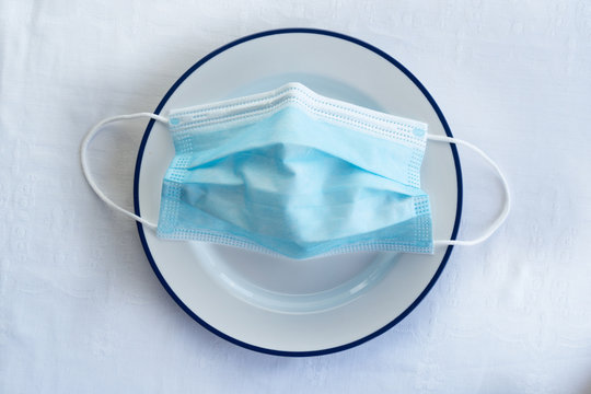 Blue Protection Face Mask For Corona Virus Or Covid 19 Prevention On White  Food Dish In Restaurant