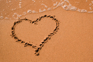 Heart drawn on sand, seacoast. Golden sand beach close up, summer holidays border frame concept.