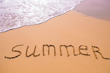 Word Summer hand written in the sand with a sea wave. Close up sand texture on beach in summer.