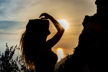 silhouette di donna altra tramonto che si passa la mano nei capelli e con i raggi del sole sul...
