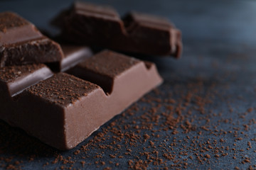 Delicious milk chocolate and cocoa powder on black table, closeup